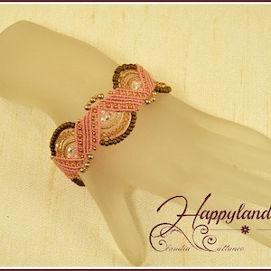 Peut inclure: Un bracelet rose et marron avec un motif géométrique et des cristaux transparents. Le bracelet est sur une main de mannequin.