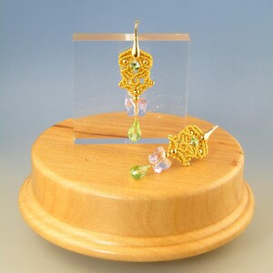May include: A pair of gold earrings with a delicate, intricate design. The earrings feature a yellow and green color scheme with a butterfly charm dangling from each earring.
