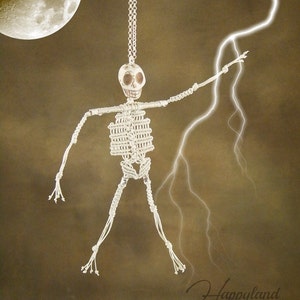 Peut inclure: Un squelette en macramé blanc suspendu à une chaîne argentée sur un fond brun avec un motif d'éclair blanc. Le squelette a un crâne blanc avec des yeux noirs.
