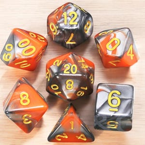 May include: A set of seven black, orange, and silver dice with yellow numbers. The dice are in a variety of shapes and sizes.
