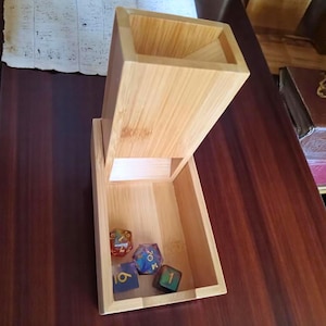 May include: A light-coloured bamboo dice tower with an open top and a tray at the bottom. Four multi-sided dice in various colours are inside the tray. The tower is made of bamboo.