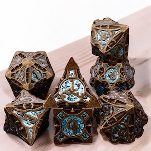 May include: Set of seven metal dice with a bronze and blue iridescent finish. The dice are detailed with intricate designs and feature numbers 1 through 6.