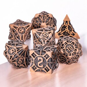 May include: A set of seven metal dice with a black and gold finish. The dice are detailed with intricate designs and feature a variety of numbers.