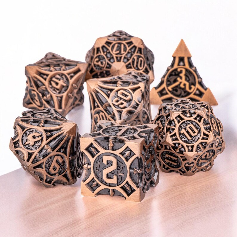 May include: A set of seven metal dice with a black and gold finish. The dice are detailed with intricate designs and feature a variety of numbers.