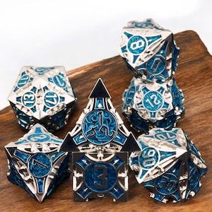 May include: Set of six silver and blue metal dice with intricate designs and numbers. The dice are on a wooden surface.