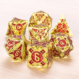 May include: Set of seven gold and red metal dice with a detailed design. The dice are numbered 4, 6, 8, 10, 12, and 20.