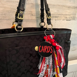 May include: Black tote bag with a black and white patterned design. The bag has a gold zip and a black leather strap. A black and red keychain with the word "CARDS" is attached to the bag.