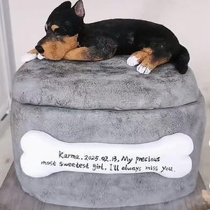 May include: A grey pet urn with a sculpted dog figurine on top. The urn has a bone-shaped plaque with the inscription "Karma, 2025.02.13, My precious most sweetest girl, I'll always miss You."