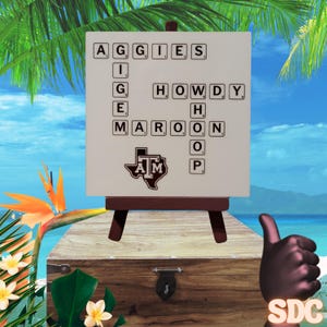 May include: A white board with a crossword puzzle featuring the words "Aggies", "Howdy", "Maroon", and "Gig 'em". The board is on a wooden easel and has a Texas A&M logo in the bottom center.