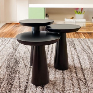 Puede incluir: Tres mesas de centro de madera negra con tapas redondeadas. Las mesas están dispuestas en forma escalonada sobre una alfombra estampada.