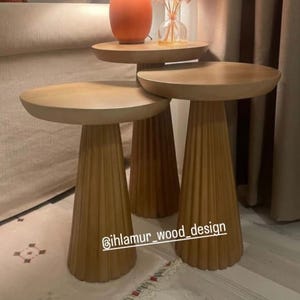 Puede incluir: Tres mesas auxiliares de madera en color marrón claro. Las mesas tienen una tapa redonda y una base cónica acanalada. Son de diferentes alturas, una de ellas soporta una lámpara y un jarrón. El texto "@ihlamur_wood_design" es visible.
