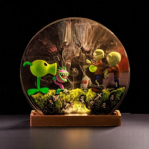 May include: A circular glass terrarium with a Plants vs. Zombies theme. It contains a green Peashooter, a pink Piranha Plant, and two zombie figures. The base is wooden, and the background has a smoky effect. The scene is illuminated.