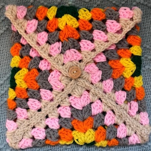 May include: A colorful crocheted square with a brown button that says "Handmade with Love". The square is made with pink, orange, yellow, green, and gray yarn.
