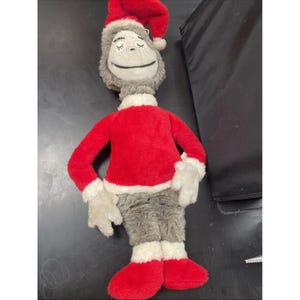 May include: A plush doll of a character with a gray face and body, wearing a red Santa-style outfit with white trim. The doll has a red hat and closed eyes, and red feet. The doll is approximately 24 inches tall.