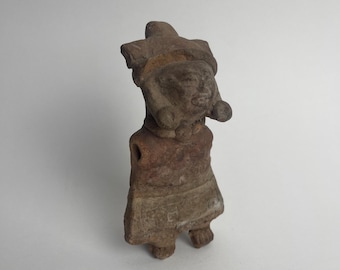 May include: A small, brown clay figurine of a person wearing a headdress. The figurine has a simple, stylized design and is likely from an ancient culture.