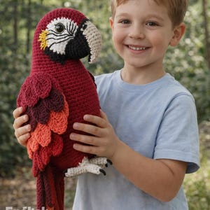 May include: A handmade, crocheted parrot in shades of red, orange, and brown. The bird has a white and black head with yellow accents. The image includes the text "PDF PATTERN" and "English Pattern".