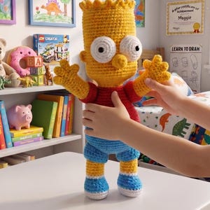 May include: A handmade crochet Bart Simpson doll, featuring a yellow head with spiky hair, a red shirt, and blue shorts. The doll has large white eyes and is posed with arms outstretched. The background includes framed artwork and a bookshelf.