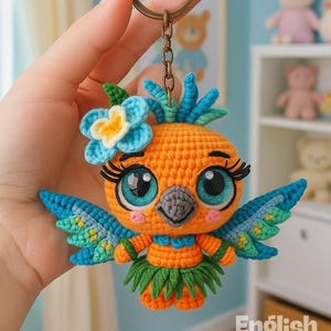 Könnte beinhalten: Ein gehäkelter Vogel-Schlüsselanhänger in Orange, Blau und Grün. Der Vogel hat große, ausdrucksstarke Augen, eine Blume auf dem Kopf und einen grünen Rock. Der Schlüsselanhänger ist an einem bronzefarbenen Ring befestigt. Der Text auf dem Bild lautet "PDF PATTERN" und "English Pattern".