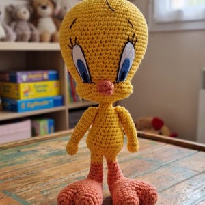 May include: A handmade crochet Tweety Bird doll. The yellow bird has blue eyes, an orange beak and feet. The doll is standing on a wooden table. The words "PDF PATTERN" and "English Pattern" are visible.