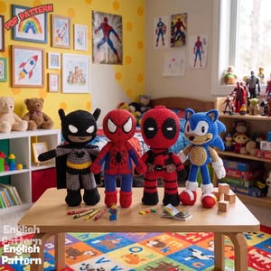 May include: Four handmade crochet dolls representing Batman, Spider-Man, Deadpool, and Sonic the Hedgehog stand on a light wood table. Each figure features detailed yarn stitching, iconic character colours, and distinct facial features. A small plastic figure and crayons are also on the table.
