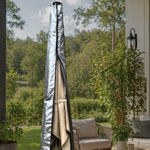 Può includere: Una copertura argentata per ombrellone da esterno con cerniera nera. La copertura protegge un ombrellone da patio beige. Lo sfondo mostra un'ambientazione da patio con alberi e mobili da esterno.