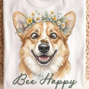 May include: White t-shirt featuring a watercolor illustration of a smiling Corgi wearing a floral crown and a bee on its nose. The text "Bee Happy" is written in green script below the dog.