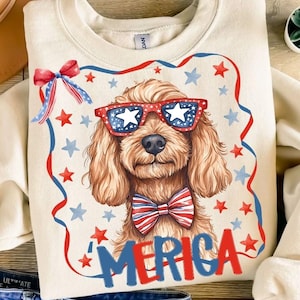 May include: A cream-colored crewneck sweatshirt featuring a graphic of a brown dog wearing star-patterned sunglasses and a red, white, and blue striped bow tie. The design includes a red and blue ribbon border, stars, and the text MERICA.