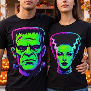 May include: Two black t-shirts featuring vibrant neon-style graphic prints. One shirt displays a green-toned Frankenstein monster with neck bolts, while the other features a green-toned Bride of Frankenstein with a signature tall hairstyle.