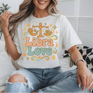 以下が含まれることがあります： レトロなスタイルで、天秤座の星座のシンボルと「Libra Love」のテキストが描かれた白いTシャツです。