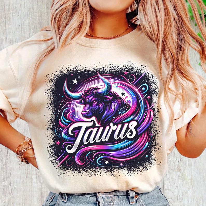 May include: A white t-shirt with a colourful graphic design featuring a bull's head and the word "Taurus" in a stylised font. The design is set against a black background with stars and swirls.