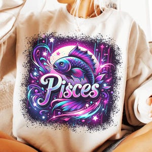 May include: A white sweatshirt featuring a colourful graphic design of a fish and the word "Pisces" in a stylised font. The design is set against a dark purple background with stars and swirls.