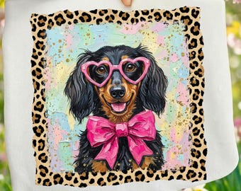 Può includere: Un cuscino quadrato bianco con un'illustrazione colorata di un bassotto con occhiali rosa a forma di cuore e un papillon rosa. L'immagine è incorniciata da un bordo leopardato.