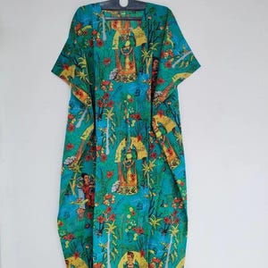 Könnte beinhalten: Ein türkisfarbener Kaftan mit einem lebendigen Blumen- und Figurenprint. Das Design zeigt rote Blumen, Palmen und Figuren in Gelb und Orange. Der Kaftan hängt an einem schwarzen Kleiderbügel.