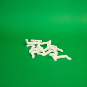 May include: A pile of white plastic hooks, likely for hanging curtains or other household items, against a green background.