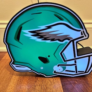 May include: A green and white football helmet with a black and gray wing design. The helmet is a decorative light fixture.