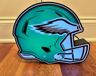 May include: A green and white football helmet with a black and grey wing design. The helmet is a decorative light fixture.