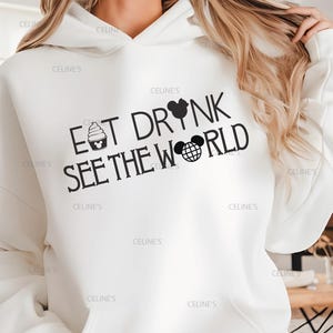 May include: White hoodie with the text "EAT DRINK SEE THE WORLD" in black. The design includes a cupcake, a Mickey Mouse head, and a globe. The hoodie has a hood and long sleeves.