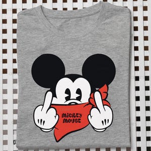 Może przedstawiać: Szary melanżowy t-shirt z grafiką czarno-białej postaci Myszki Miki z czerwoną bandaną na twarzy. Postać jest przedstawiona z obiema rękami uniesionymi do góry, pokazującymi środkowe palce. Napis Mickey Mouse jest w kolorze czarnym.