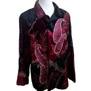 May include: A long-sleeved shirt with a patchwork design. The shirt features a black velvet collar and panels, with burgundy and maroon paisley and floral embroidery. The shirt has a button-down front and long sleeves.