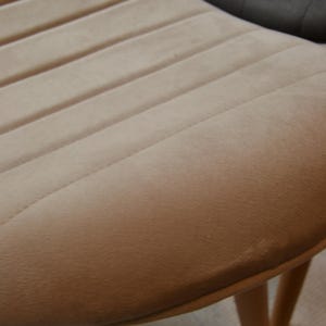 May include: A beige velvet chair with a rounded back and wooden legs. The chair has a tufted design on the back.