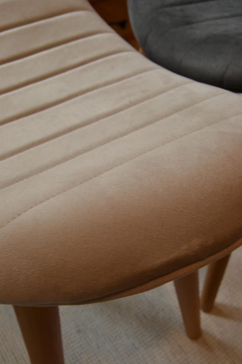 May include: A beige velvet chair with a rounded back and wooden legs. The chair has a tufted design on the back.
