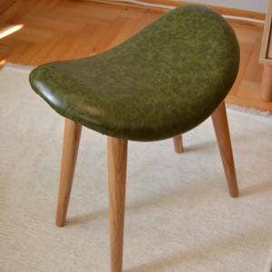 Puede incluir: Un taburete tapizado verde con un asiento curvo y cuatro patas de madera.