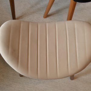 May include: A cream-coloured velvet chair seat with vertical stitching. The chair seat is oval shaped and has a smooth, soft texture.