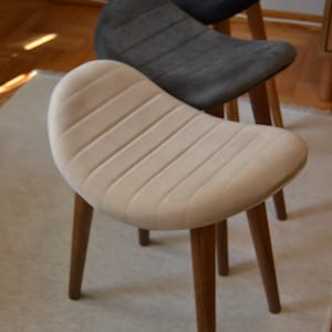 May include: Three upholstered stools with wooden legs. The stools are in different colours: beige, grey, and black. The stools are arranged in a staggered formation, with the beige stool at the front and the black stool at the back.