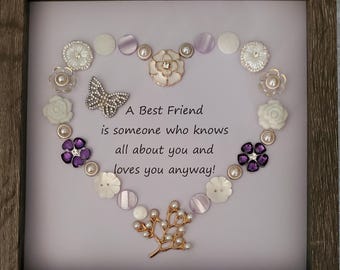 May include: Framed artwork featuring a heart-shaped arrangement of decorative buttons, pearls, and a butterfly. The text reads "A Best Friend is someone who knows all about you and loves you anyway!" The frame is a light brown color.