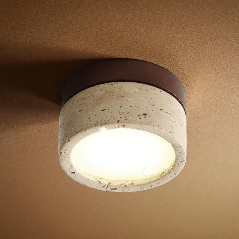 May include: A cylindrical ceiling light fixture with a brown top and a textured, off-white stone-like body. The light emits a bright glow from the recessed opening. The fixture is designed for flush mounting.
