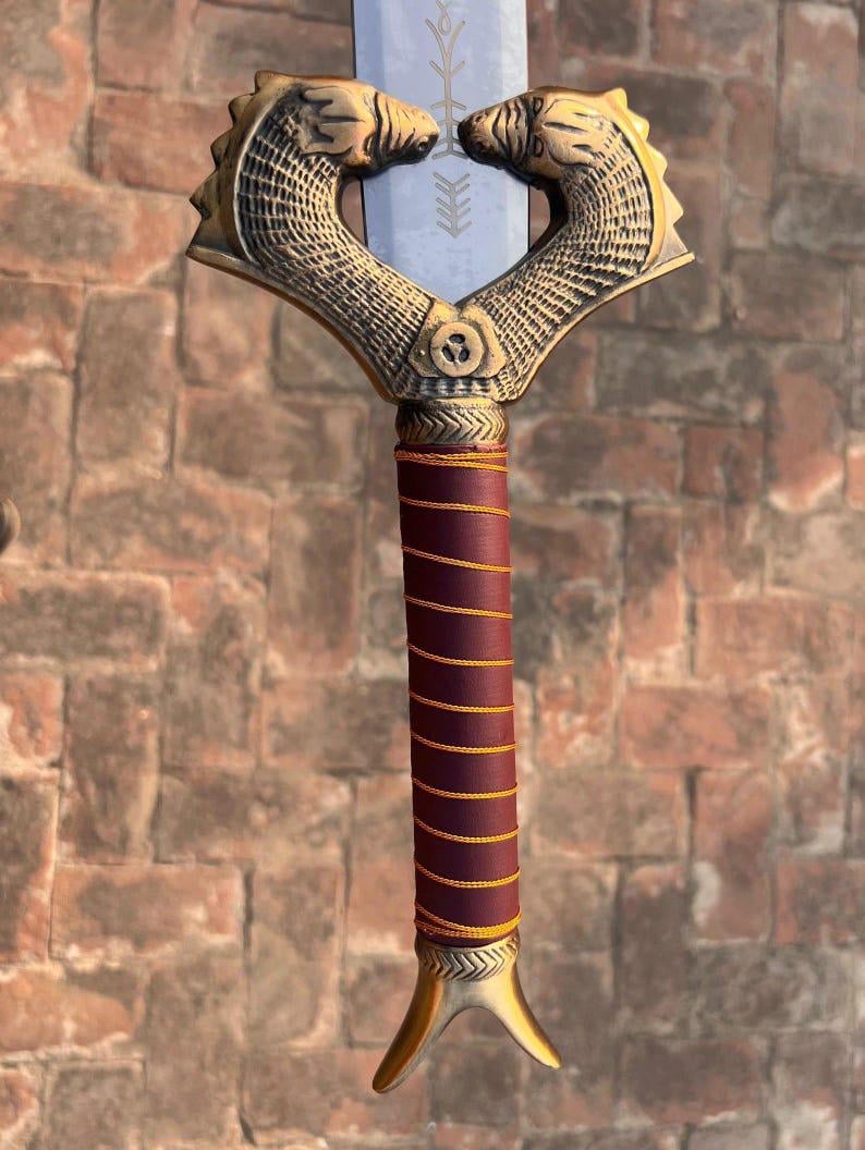 K&ouml;nnte beinhalten: Ein Schwert mit einem goldfarbenen Griff, der mit zwei stilisierten Tierk&ouml;pfen verziert ist. Der Griff ist mit burgunderfarbenem Leder mit goldenen Akzenten umwickelt. Die Klinge ist silberfarben und hat ein dekoratives Design.