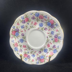 May include: A white porcelain saucer with a gold rim and a floral pattern of pink, purple, and blue sweet peas.