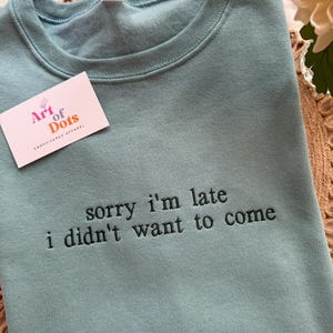 May include: A teal sweatshirt with the embroidered phrase "sorry i'm late i didn't want to come" in black thread. A small white business card with the "Art of Dots" logo is on the left side. The sweatshirt is a size L/G/G.