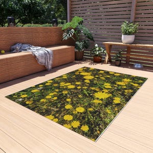 Puede incluir: Una alfombra rectangular que presenta una impresión fotográfica de alta resolución de un campo lleno de flores de diente de león de color amarillo vibrante y hierba verde, sobre un fondo oscuro y sombreado, creando un patrón floral realista.